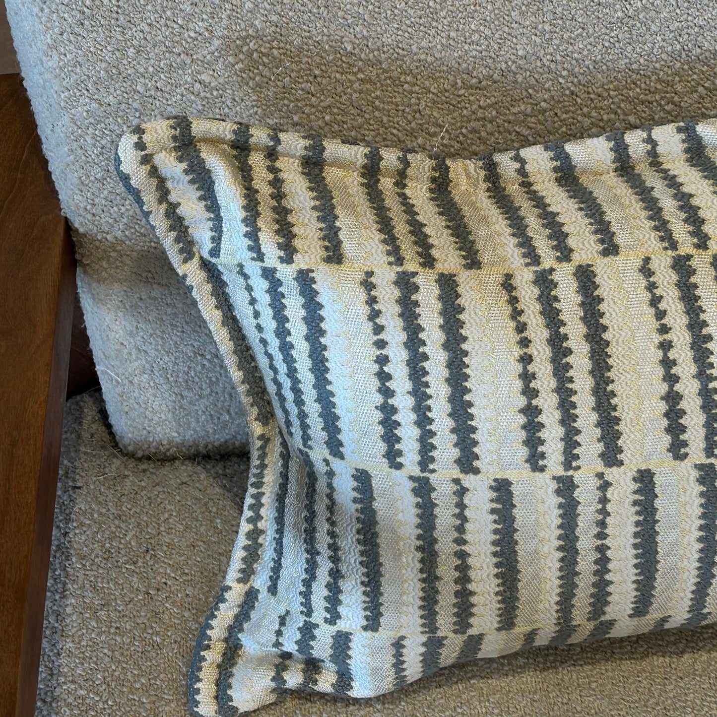 Détail d’un coussin rectangulaire à rayures graphiques gris et écru en tissu texturé, posé sur fauteuil clair