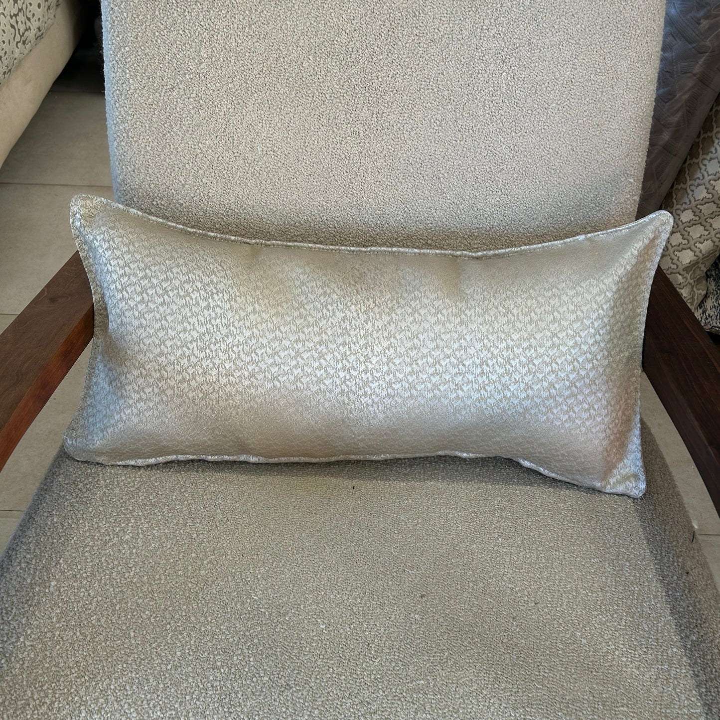 Coussin rectangulaire écru à motif discret, tissu élégant et raffiné, posé sur un fauteuil clair