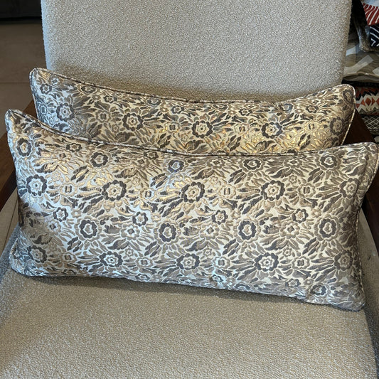 Coussins rectangulaires à motif floral taupe et bronze en tissu texturé, posés sur fauteuil clair