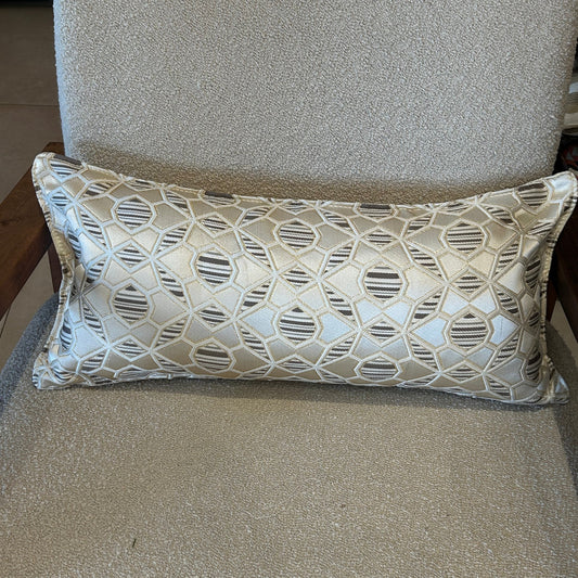 Coussin rectangulaire à motif géométrique écru et taupe en tissu texturé, posé sur fauteuil clair