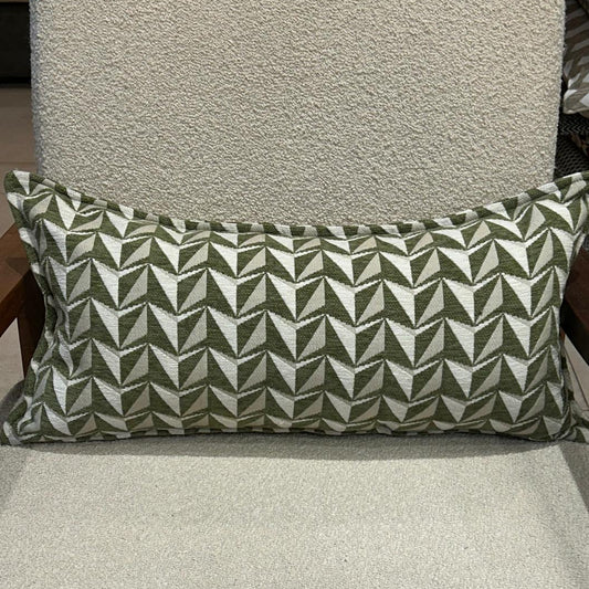 Coussin rectangulaire à motif géométrique vert et écru en tissu texturé, posé sur fauteuil clair