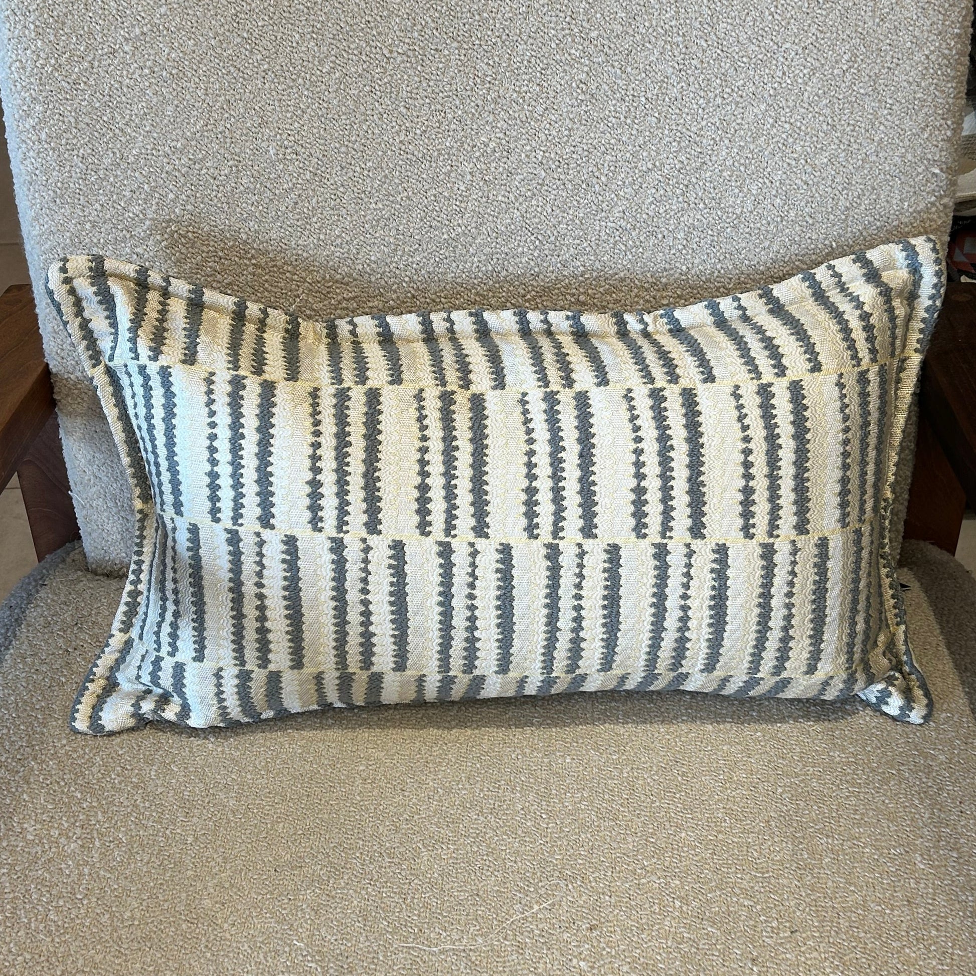 Coussin rectangulaire à rayures graphiques gris et écru en tissu texturé, posé sur fauteuil clair