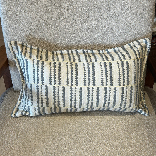 Coussin rectangulaire à rayures graphiques gris et écru en tissu texturé, posé sur fauteuil clair