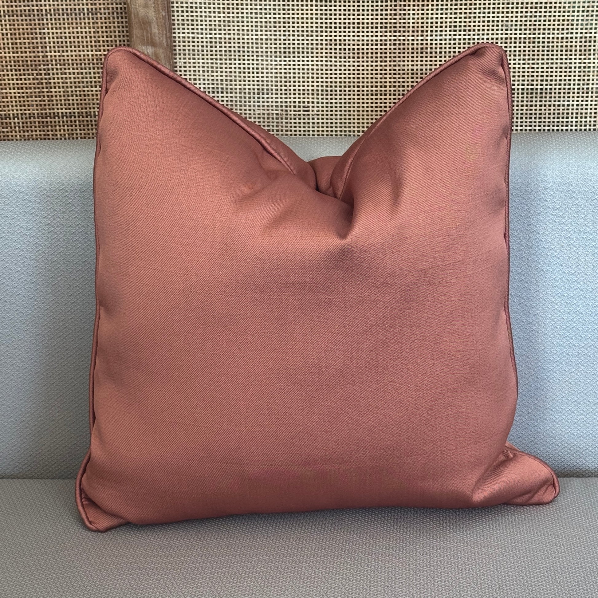 Coussin décoratif uni terracota aux tons chaleureux et raffinés, avec finition passepoil, posé sur un canapé clair dans une ambiance élégante et contemporaine.