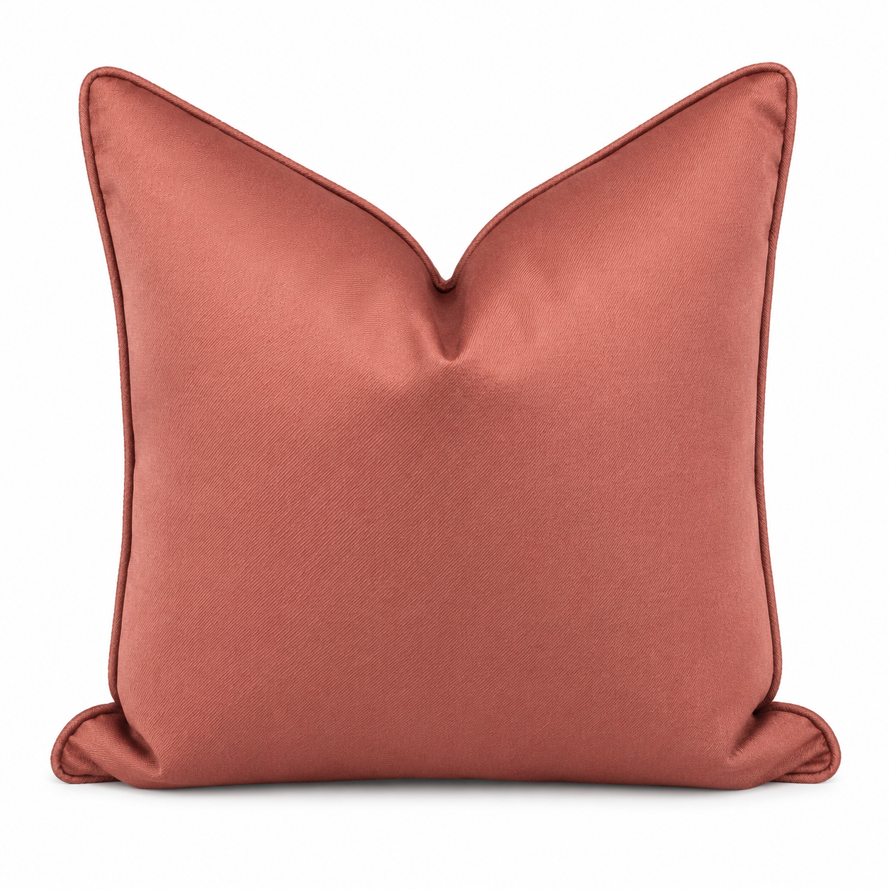 Coussin décoratif uni terracota aux tons chaleureux et raffinés, avec finition passepoil, posé sur un canapé clair dans une ambiance élégante et contemporaine.