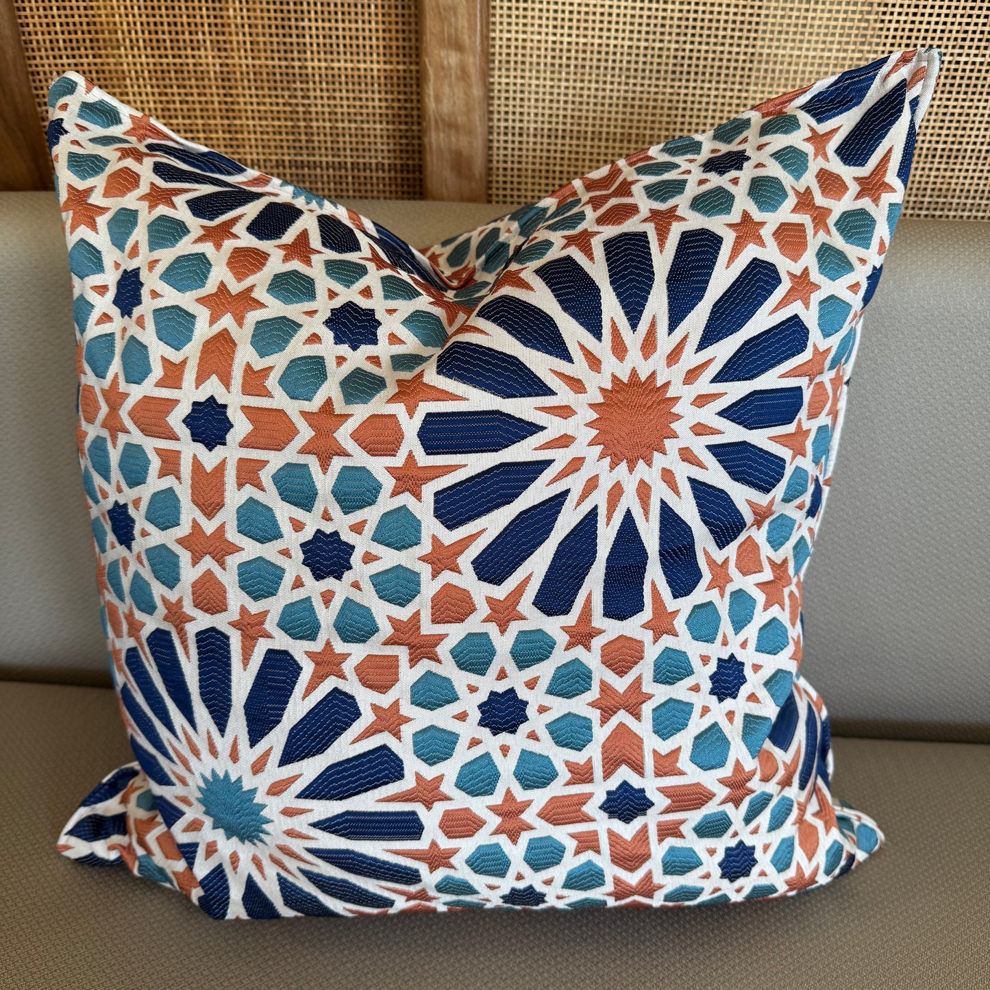Coussin décoratif à motif zellij bleu et terracotta avec effet tissé en relief, inspiré des mosaïques marocaines, posé sur une assise beige.