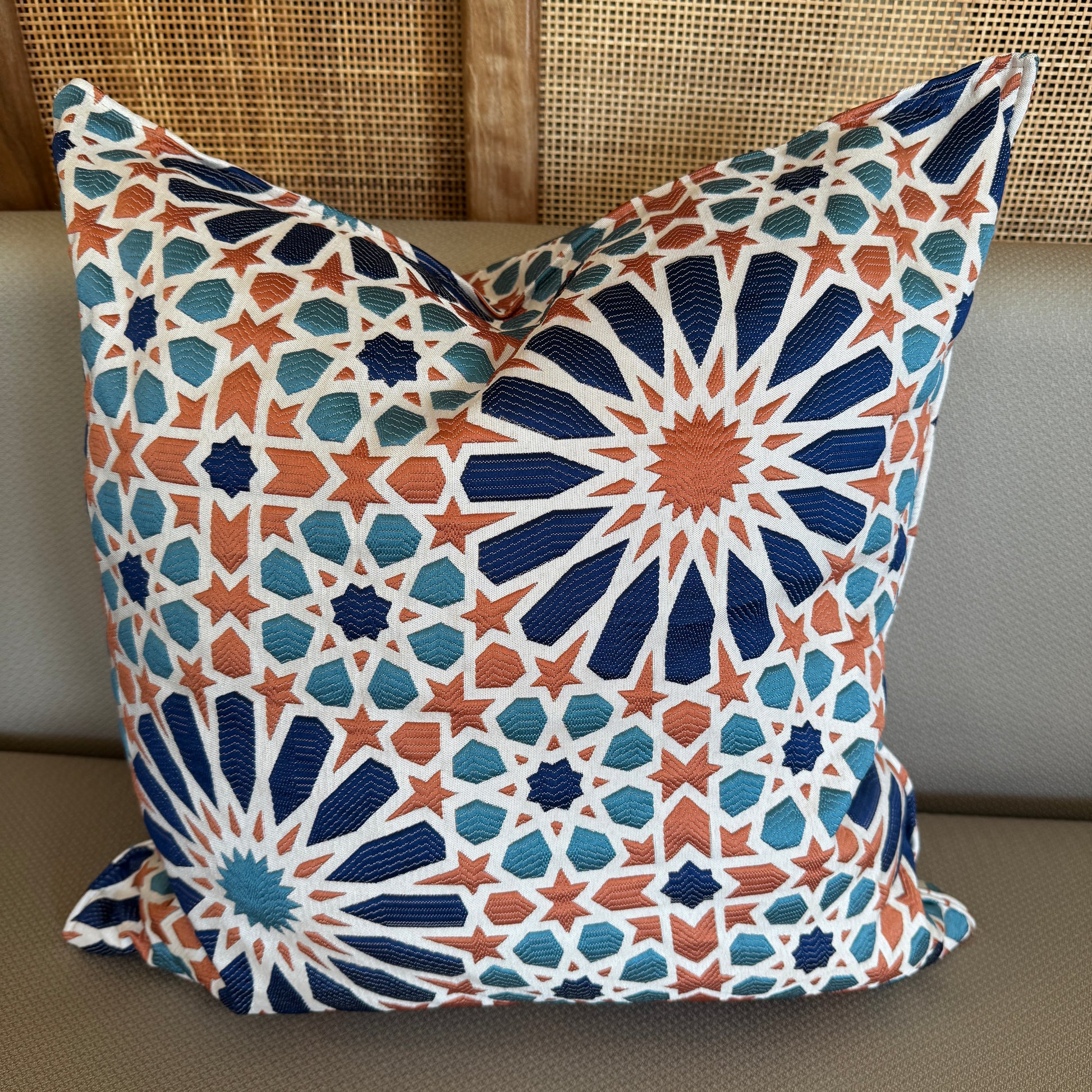 Coussin décoratif à motif zellij bleu et terracotta avec effet tissé en relief, inspiré des mosaïques marocaines, posé sur une assise beige.