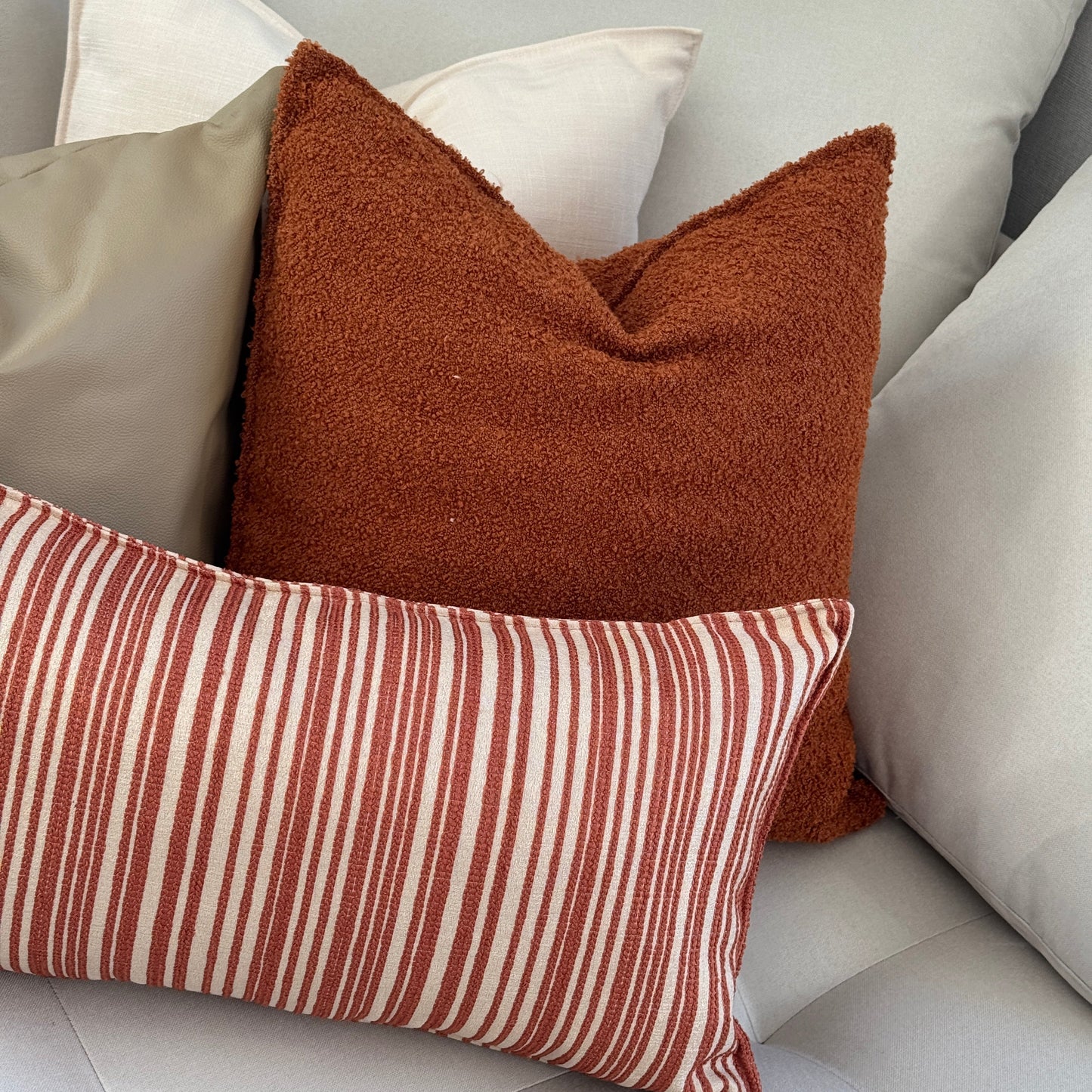 Ensemble de coussins décoratifs terracotta et beige avec coussin bouclette uni et coussin à rayures dans un salon aux tons naturels.
