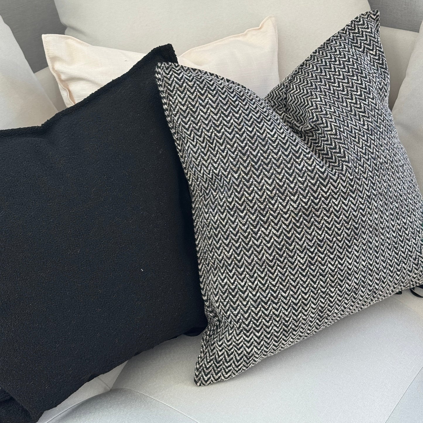 Coussins décoratifs noir et blanc avec motif chevron et coussin bouclette uni sur canapé moderne aux tons clairs.