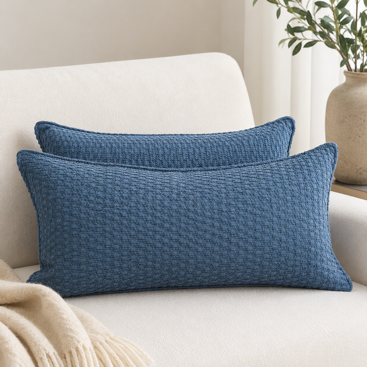 Deux coussins rectangulaires bleus texturés sur fauteuil beige dans une ambiance moderne et élégante, style décoration intérieure haut de gamme.