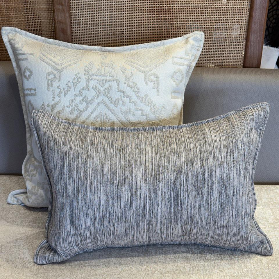 Détail de coussins décoratifs avec coussin ethnique écru à motif géométrique et coussin rectangulaire gris rayé, harmonie moderne et raffinée.