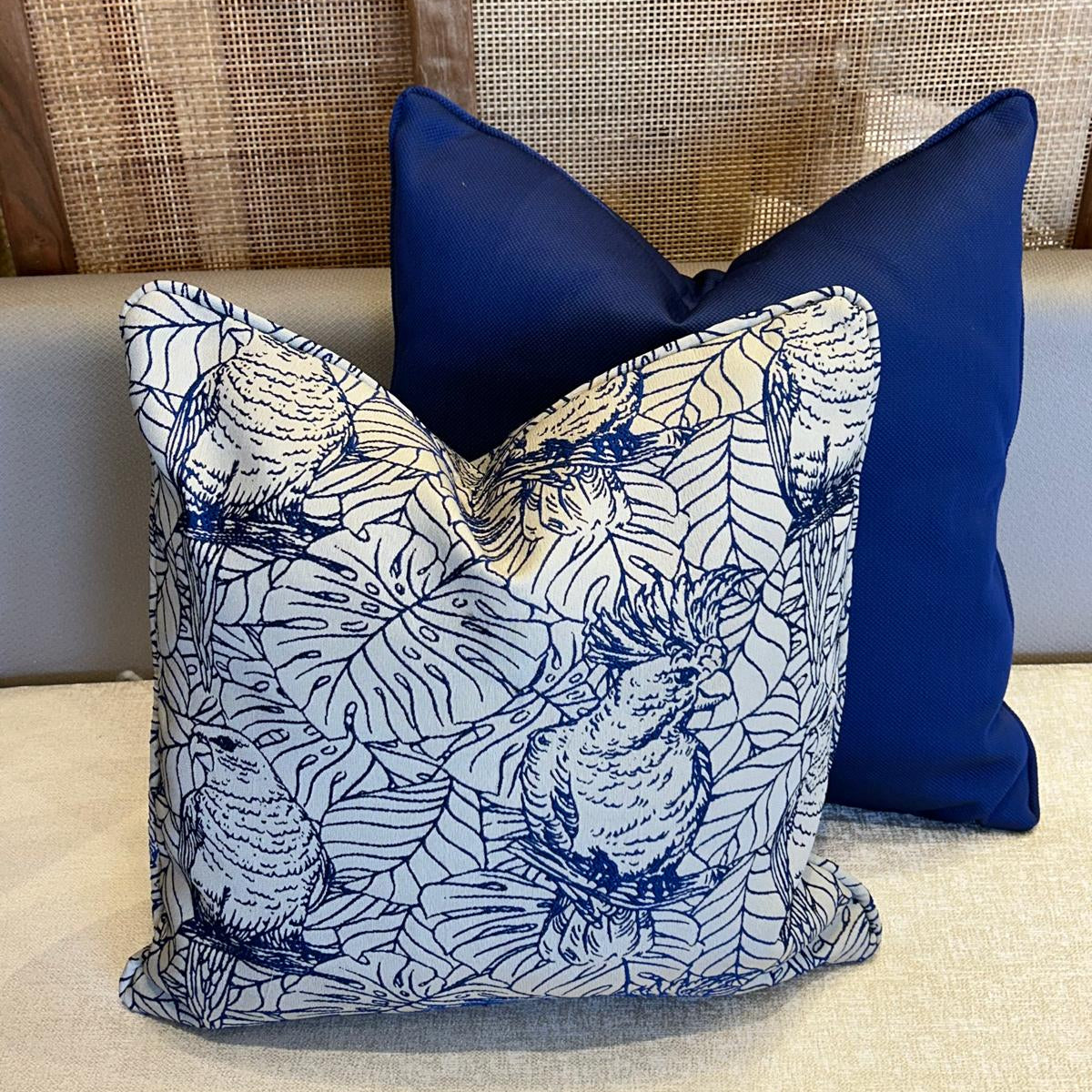 Duo de coussins décoratifs en tissu marocain : un coussin à motif oiseaux bleu et blanc et un coussin uni bleu profond, finition élégante.