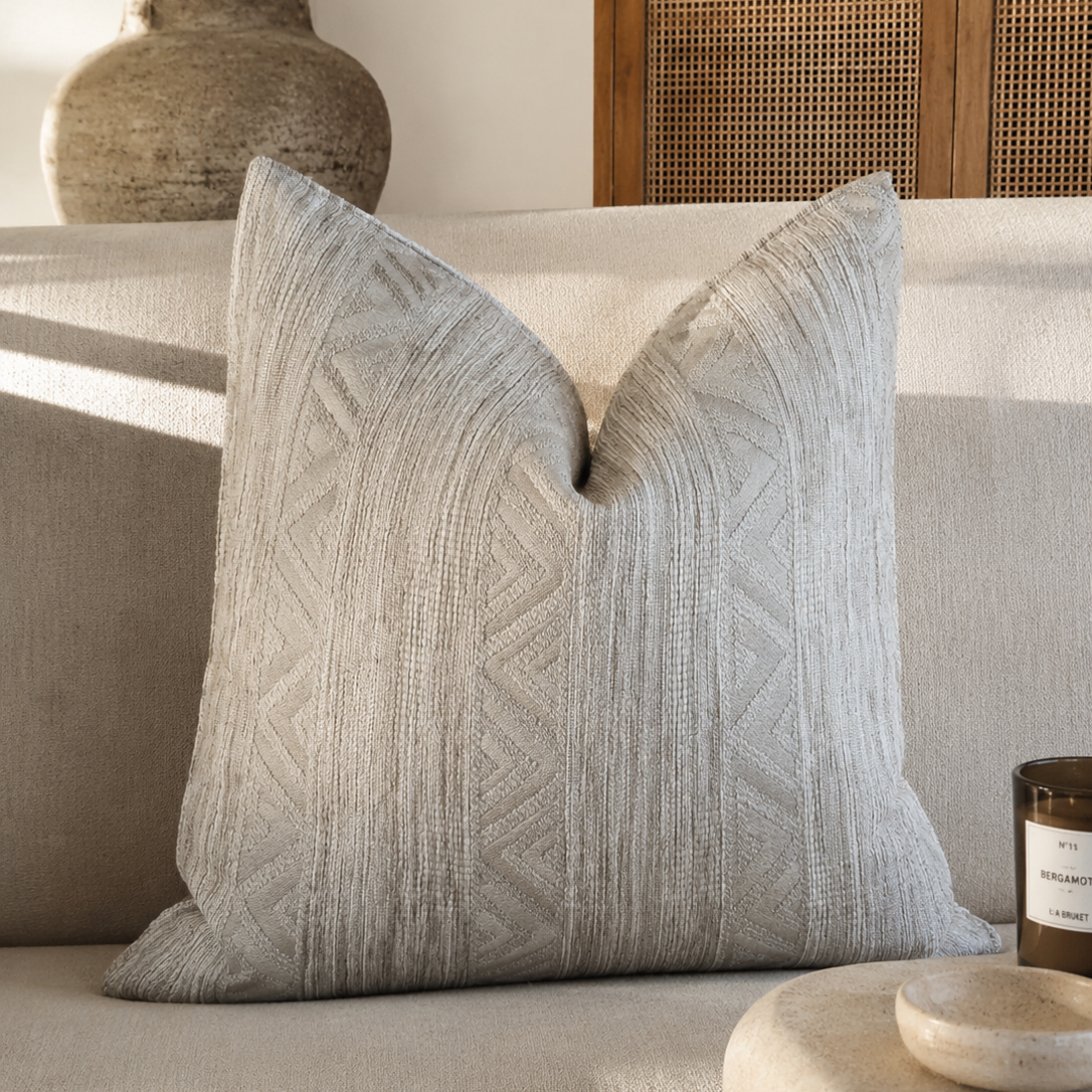 Coussin beige texturé à motifs géométriques dans une ambiance chic et néobeldi avec canapé clair et décoration naturelle élégante – Biyadi Collection.