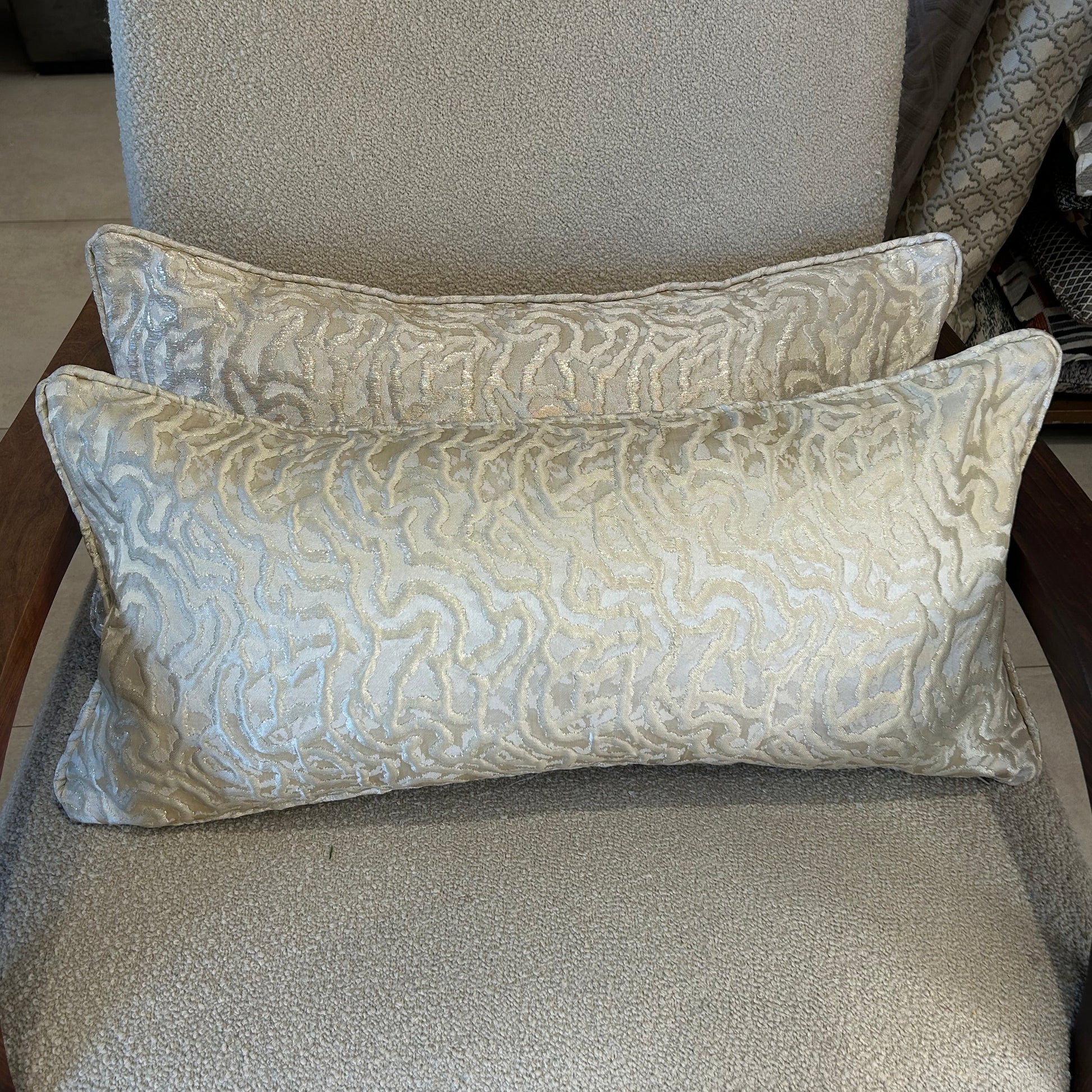 Coussin rectangulaire à motif organique beige lumineux en tissu texturé, posé sur fauteuil clair