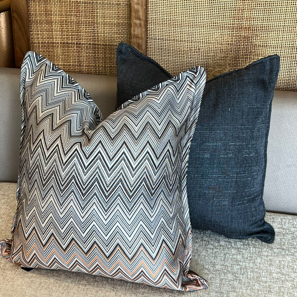 Coussin décoratif à motif zigzag gris, blanc et terracotta avec coussins unis bleu foncé sur canapé beige.