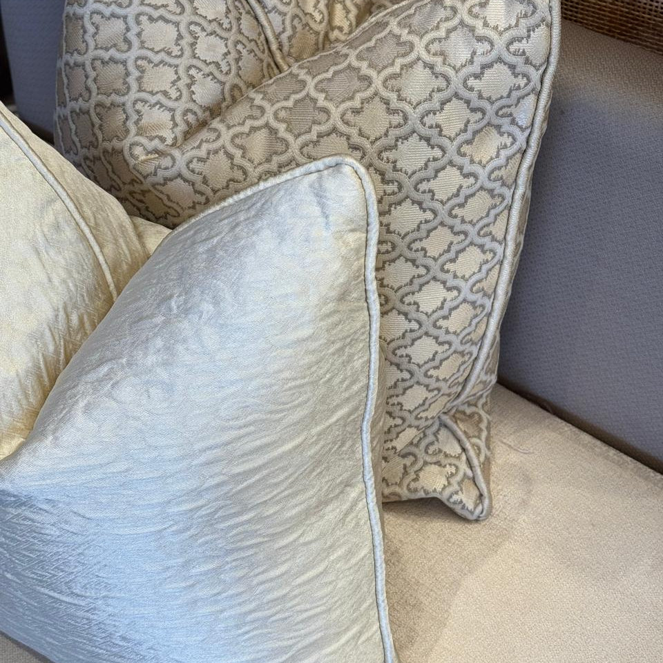 Duo de coussins décoratifs en tissus marocains : un coussin uni ivoire texturé et un coussin ethnique à motif géométrique taupe, finition haut de gamme.