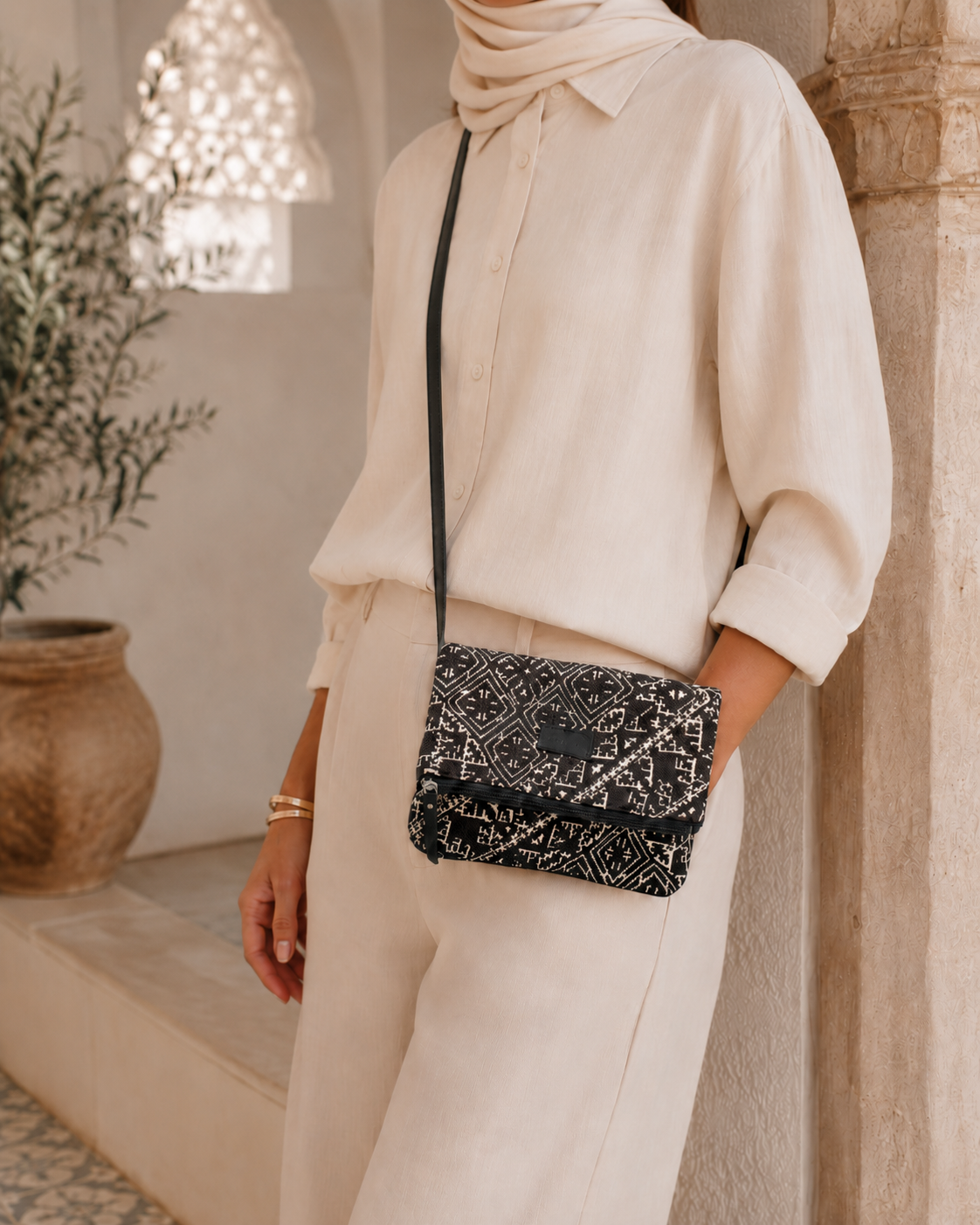 Femme en chemise écrue fermée et foulard portant un sac bandoulière noir et écru en tissu marocain Biyadi.