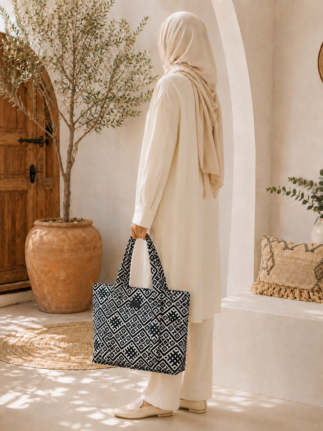 Femme en tenue écrue et foulard portant à la main un sac cabas  Rihla Biyadi bleu et écru à motif géométrique, dans une ambiance marocaine moderne.