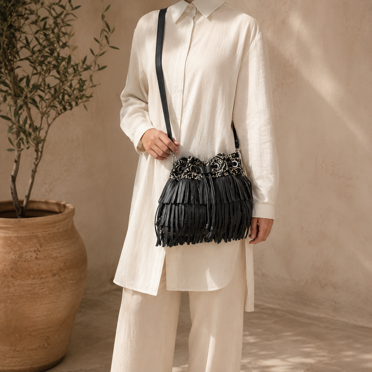 Sac seau à franges noir en tissu marocain et cuir, porté en bandoulière avec une tenue d’été élégante Biyadi Collection.