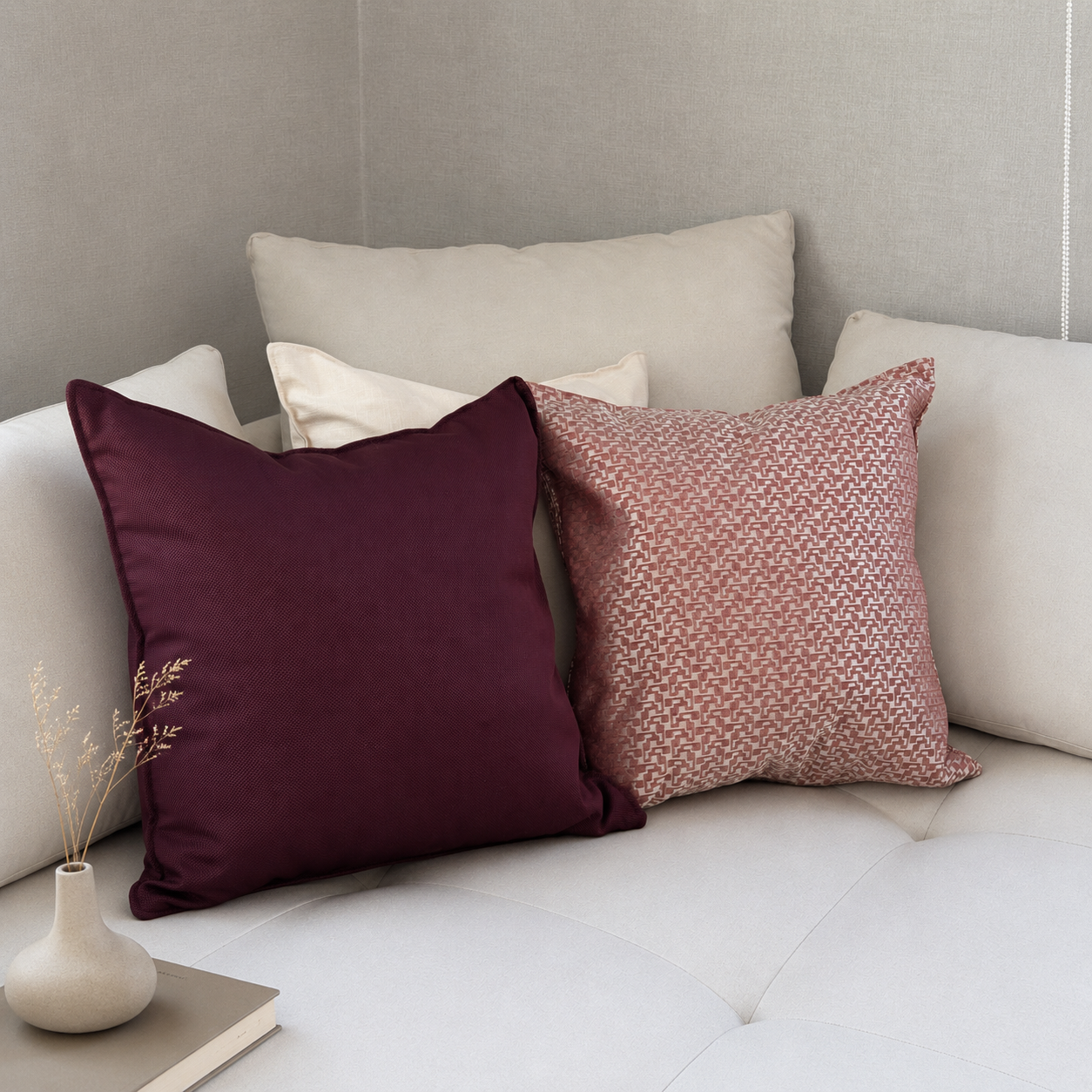 Ambiance élégante avec coussins décoratifs burgundy et vieux rose à motifs géométriques, disposés sur un canapé beige dans un intérieur moderne et raffiné.