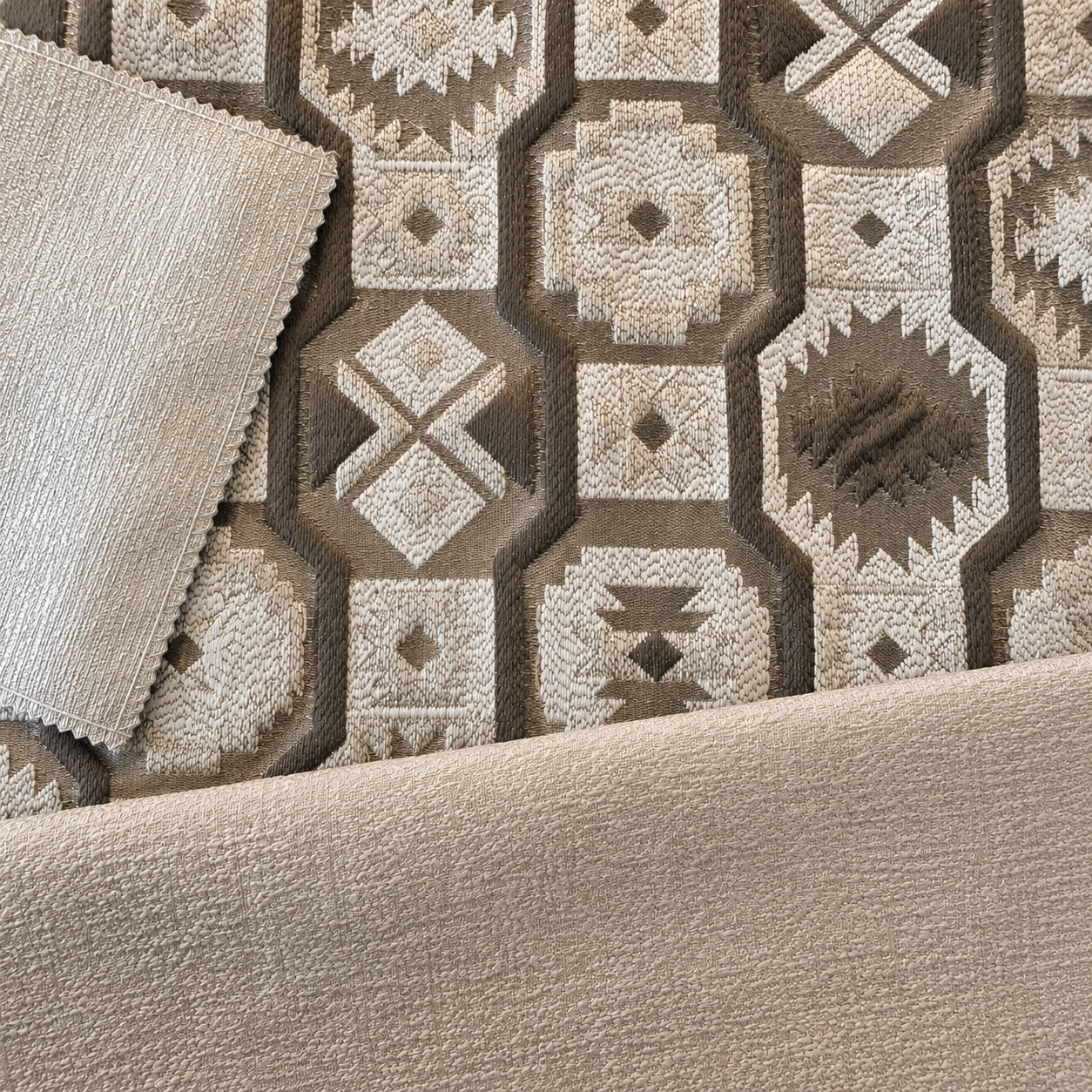 Composition de tissus d'ameublement tissés au Maroc dans des tons taupe et greige, associant un motif géométrique en relief à des tissus unis coordonnés pour salon marocain moderne.