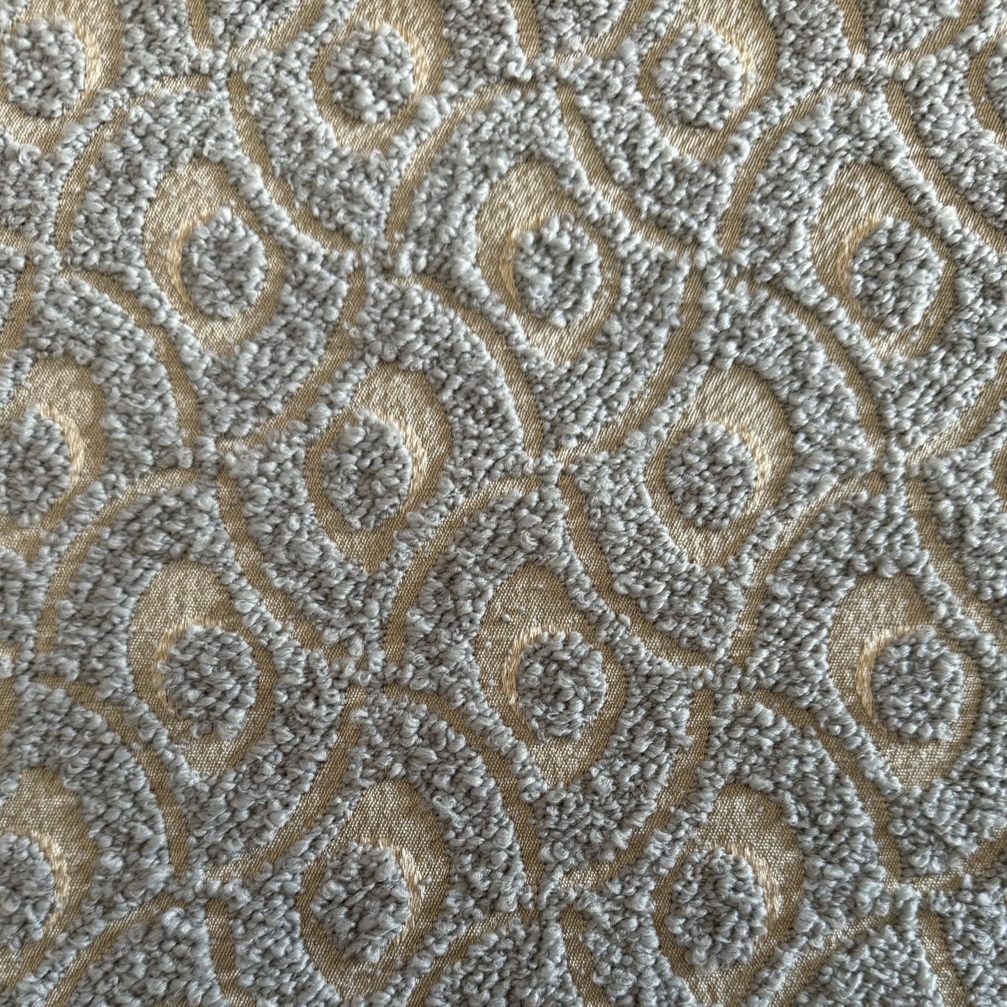 Gros plan sur un tissu bouclette gris clair à motif géométrique en relief, tissé au Maroc pour l'ameublement et la décoration intérieure.