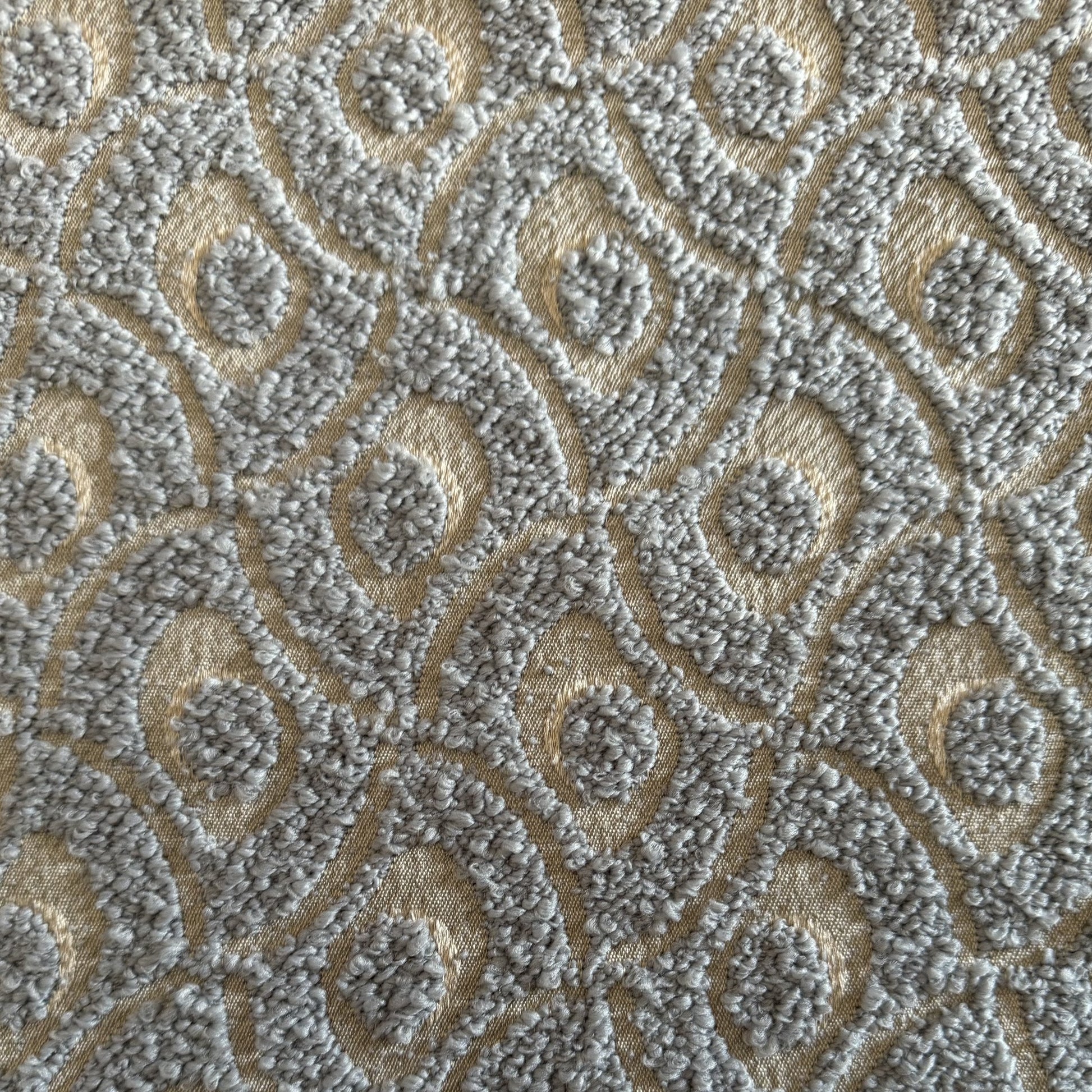 Gros plan sur un tissu bouclette gris clair à motif géométrique en relief, tissé au Maroc pour l'ameublement et la décoration intérieure.