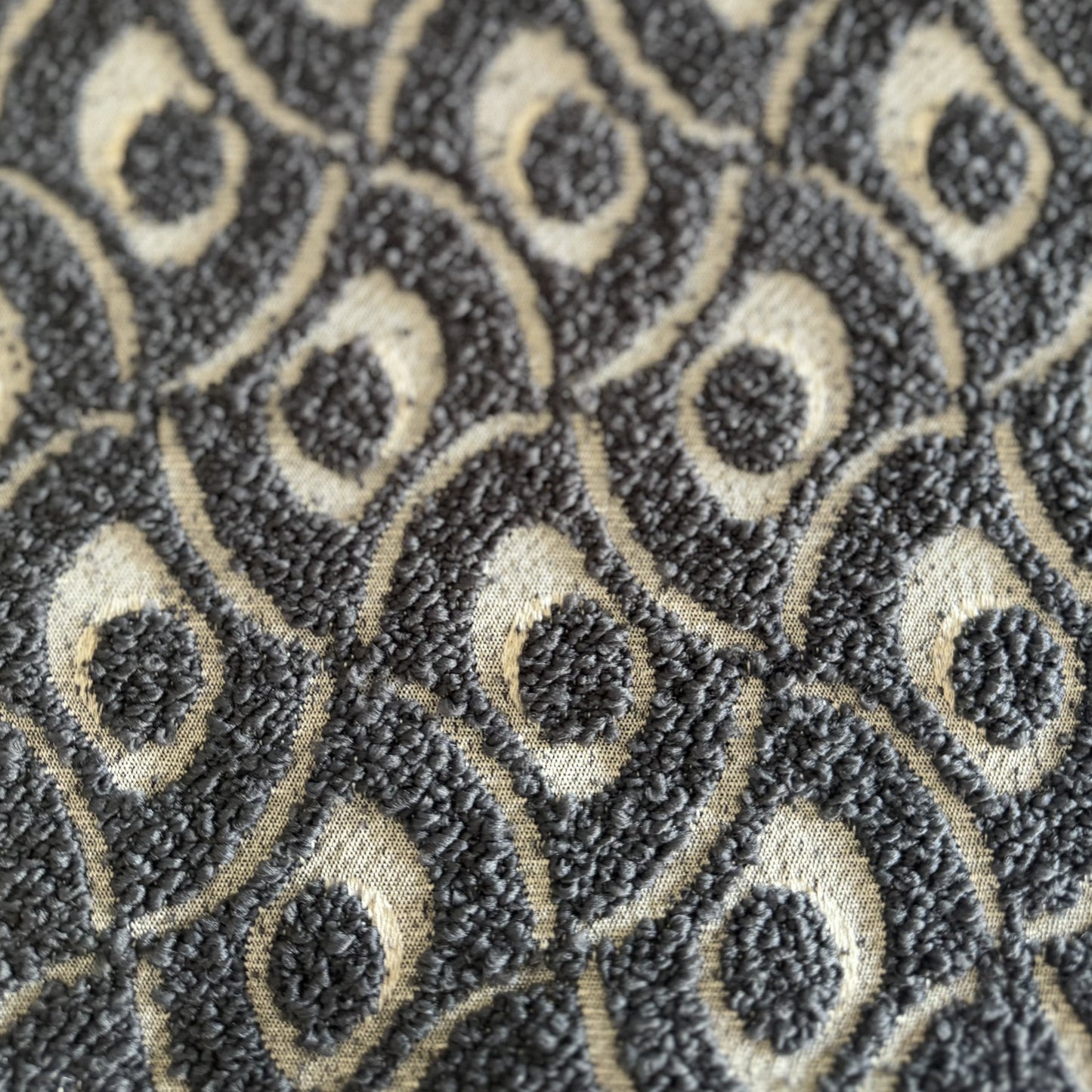 Gros plan sur un tissu bouclette gris foncé à motif géométrique en relief, tissé au Maroc pour l'ameublement et la décoration intérieure.