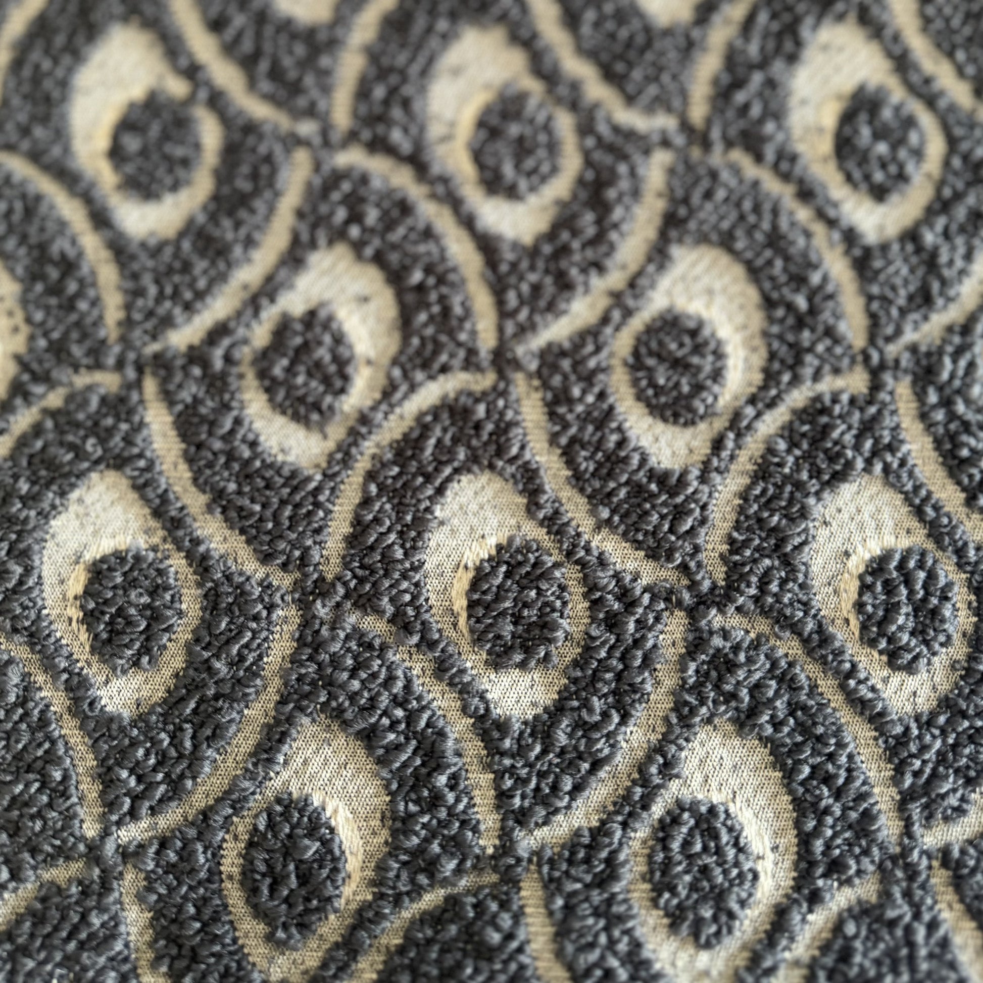 Gros plan sur un tissu bouclette gris foncé à motif géométrique en relief, tissé au Maroc pour l'ameublement et la décoration intérieure.
