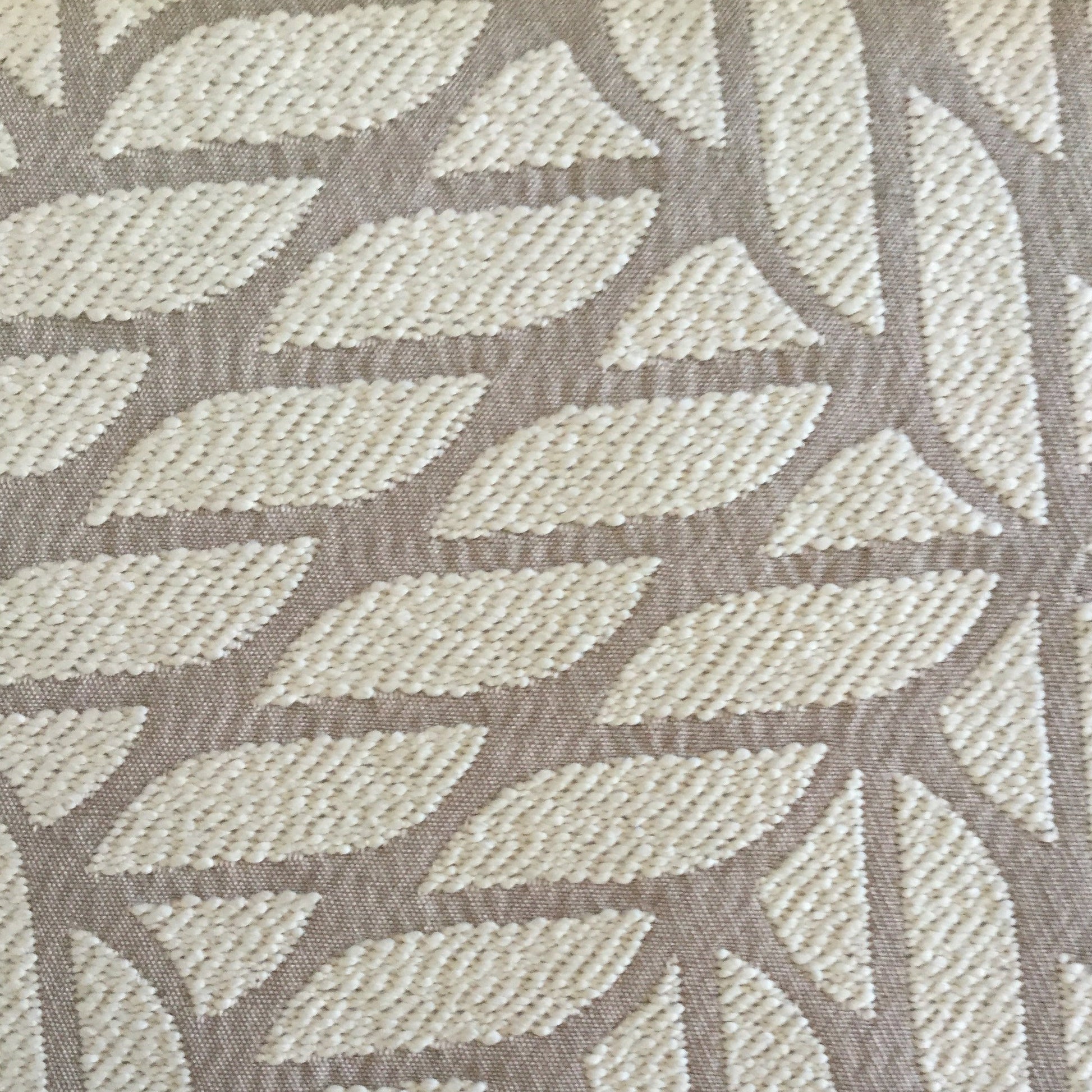 Gros plan d’un tissu d’ameublement en beige  à motif géométrique contemporain en relief, idéal pour la confection de coussins et décoration intérieure.
