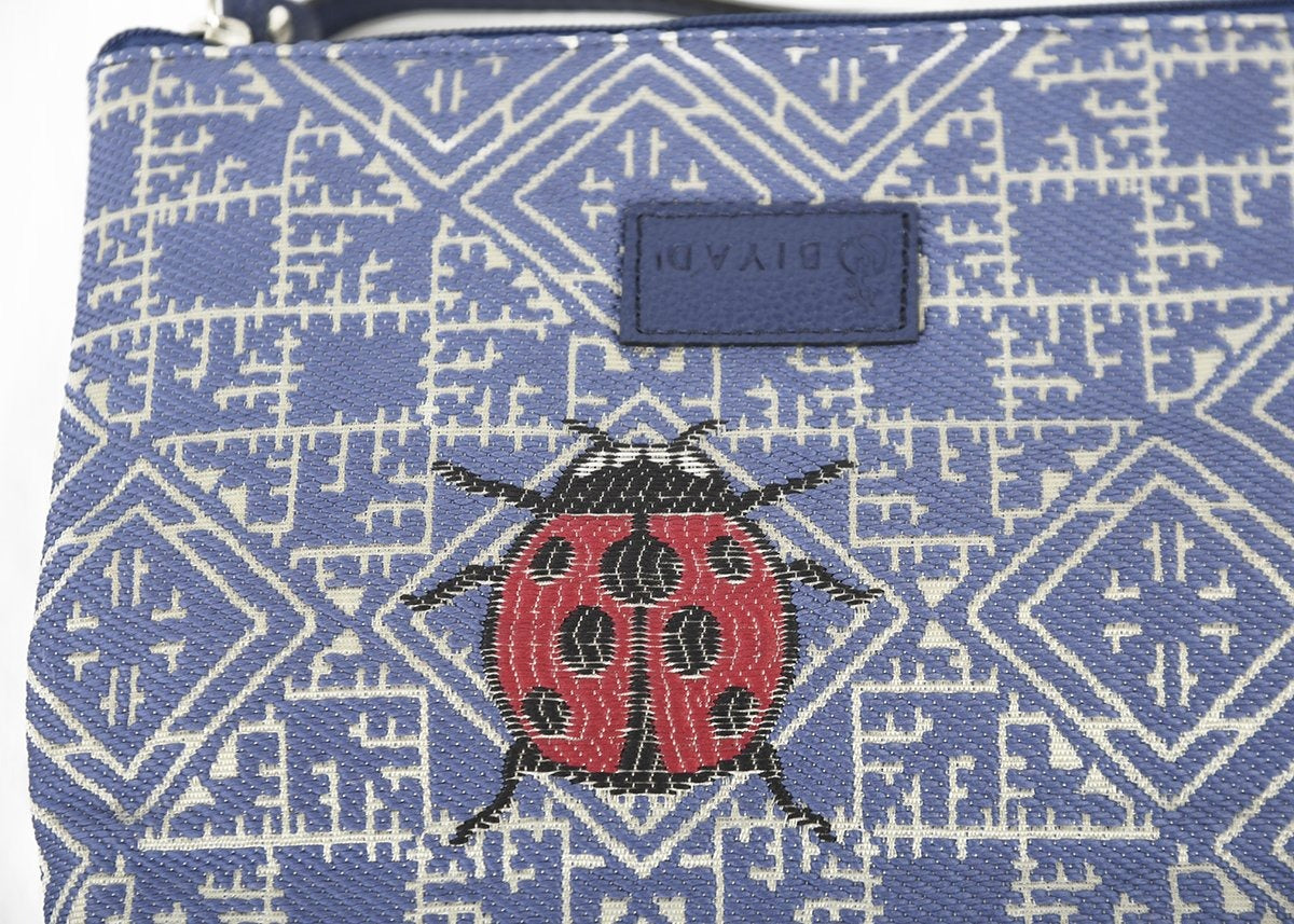 Détail d’une pochette bleu marine Biyadi Collection en tissu marocain tissé avec motif géométrique et coccinelle rouge décorative, fabriquée au Maroc.