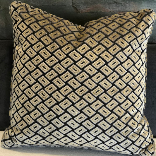 Coussin décoratif noir et écru à motif géométrique en relief, présenté sur un canapé clair dans une ambiance intérieure élégante.