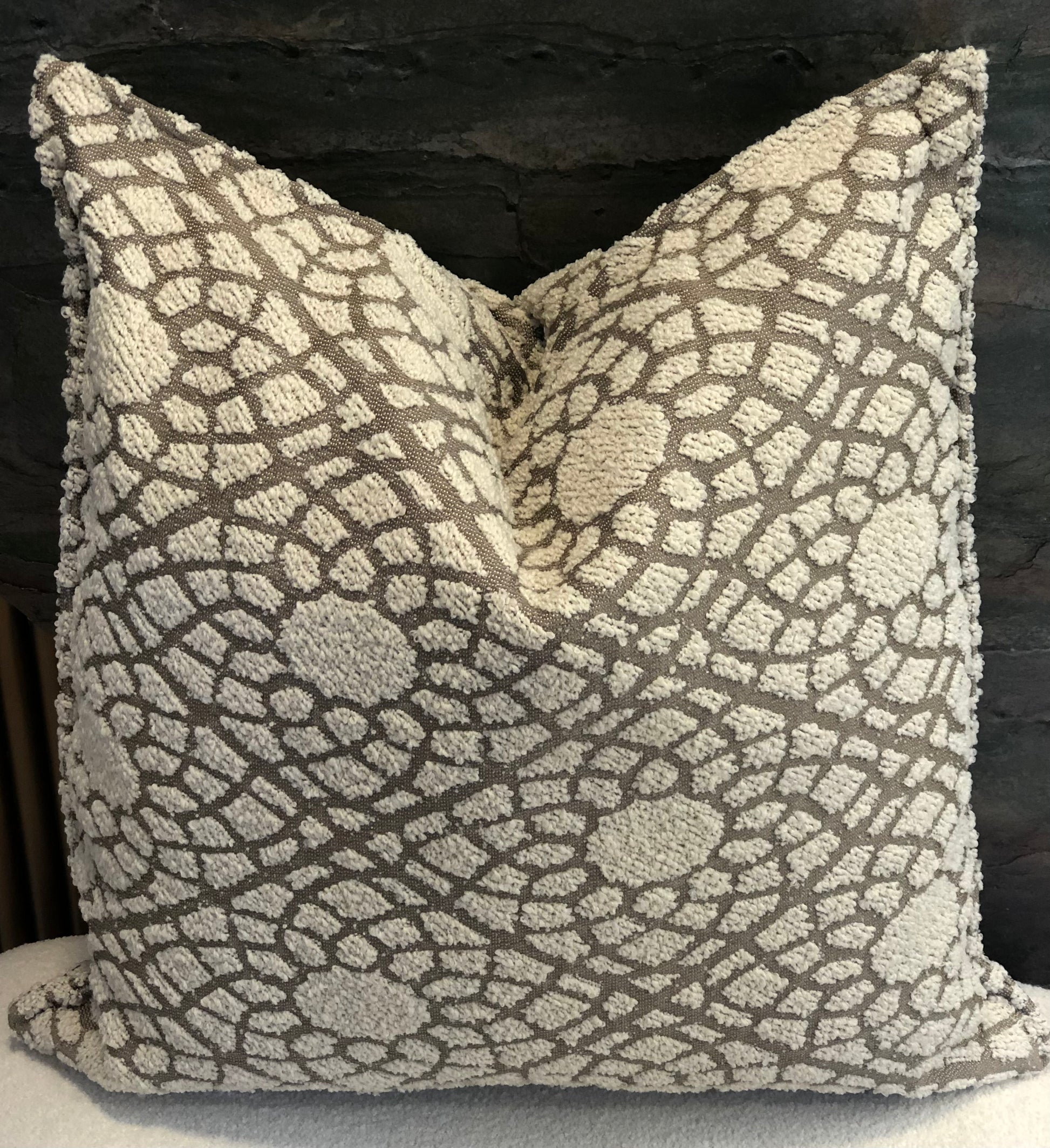 Coussin décoratif en tissu texturé à relief, motif organique écru sur fond taupe .