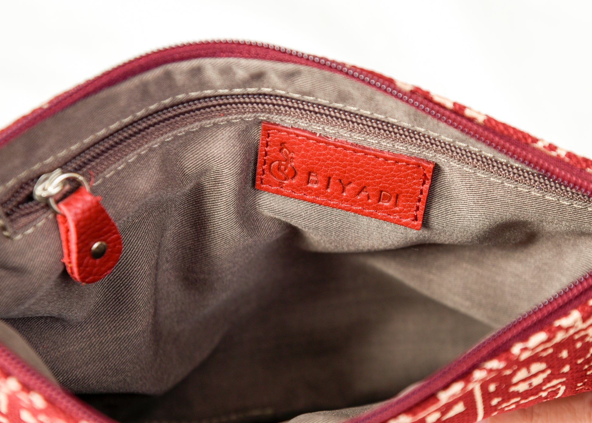 Intérieur d’une pochette bordeau à motif marocain tissé avec doublure beige, poche zippée intérieure et finitions soignées Biyadi Collection.