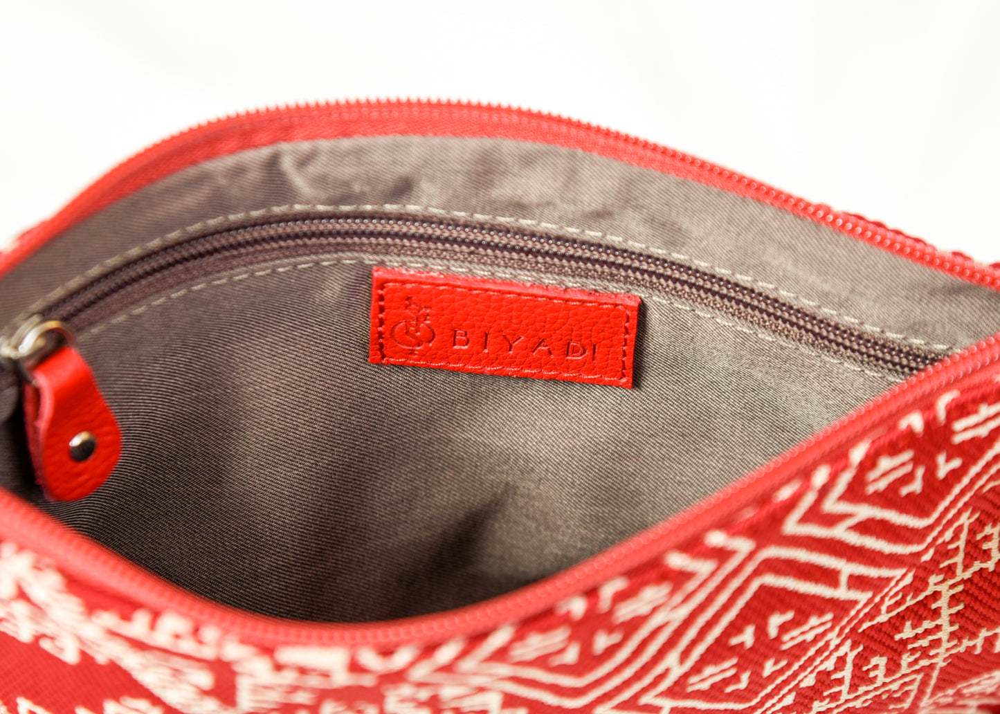 Intérieur d’une pochette rouge à motif marocain tissé avec doublure beige, poche zippée intérieure et finitions soignées Biyadi Collection.