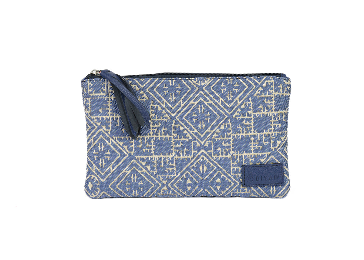 Petite pochette bleu jeans canard en tissu tissé marocain à motifs géométriques écrus, avec fermeture zippée et pompon noir décoratif.
