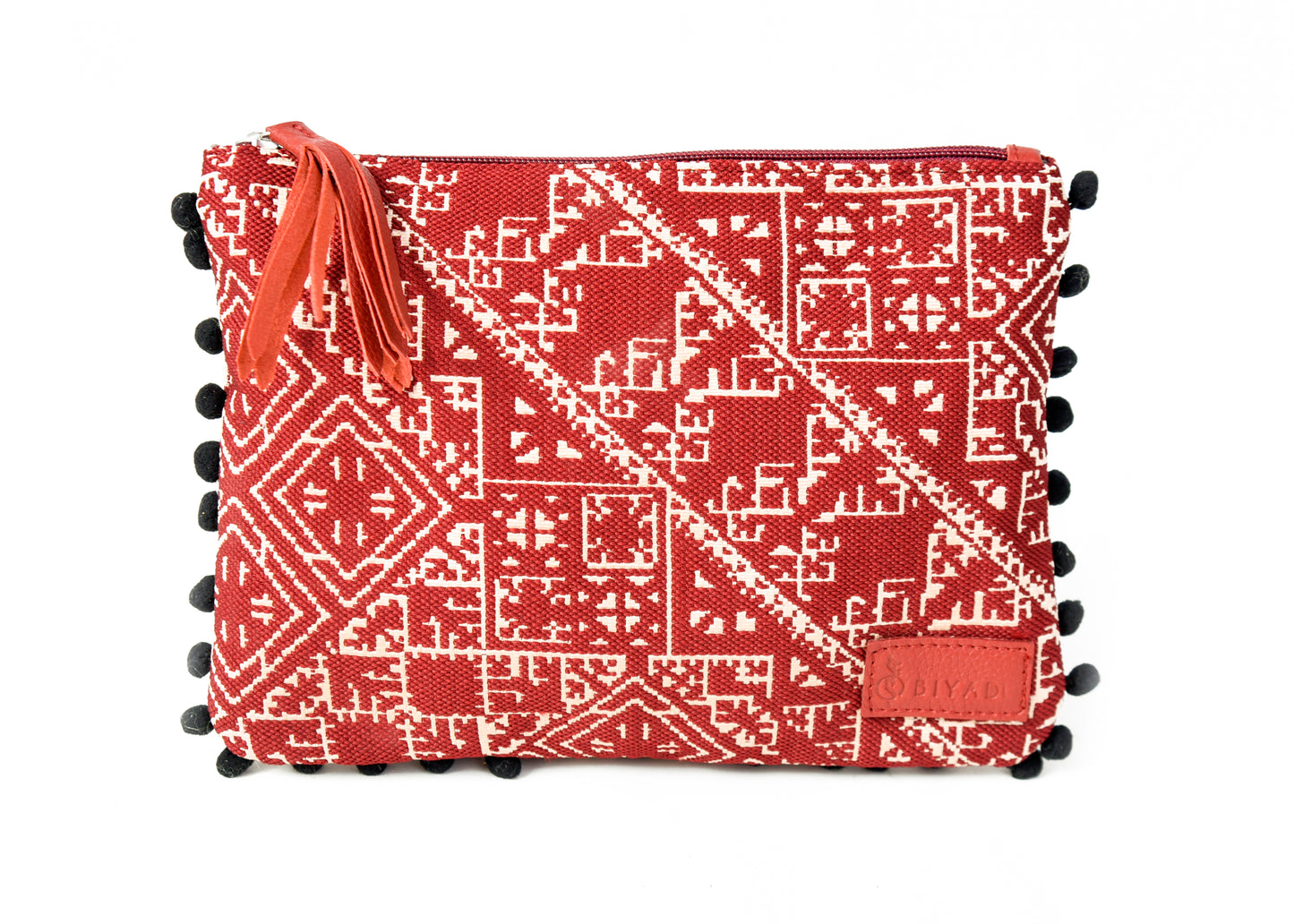 Pochette bordeau à motif marocain tissé avec pompons décoratifs et fermeture zippée, idéale pour ranger maquillage, accessoires ou essentiels du quotidien, création Biyadi Collection.