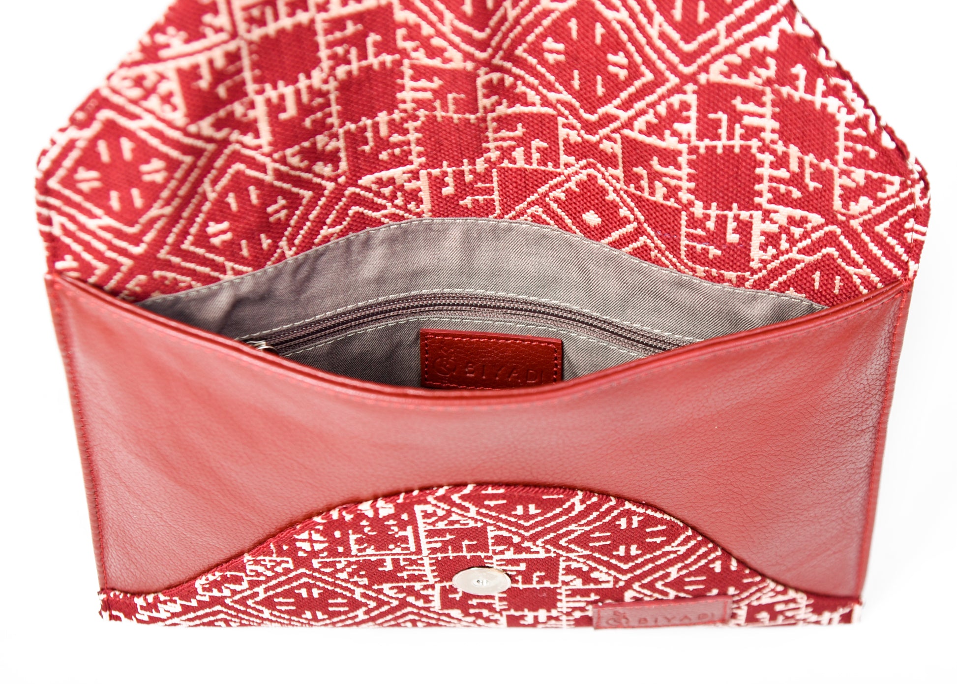 Pochette enveloppe rouge en cuir et tissu tissé marocain à motifs géométriques écrus, vue intérieure avec compartiment doublé et poche zippée.