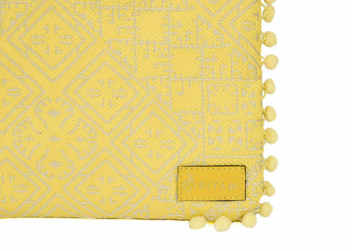 Détail d’une pochette jaune à motif marocain tissé avec pompons décoratifs et logo Biyadi, confectionnée dans un tissu exclusif tissé au Maroc.