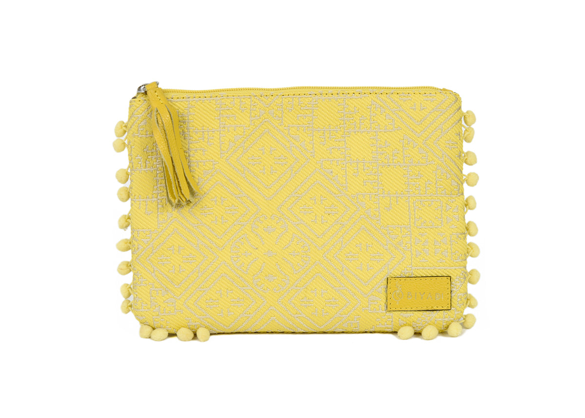 Pochette jaune à motif marocain tissé avec pompons décoratifs et fermeture zippée, idéale pour ranger maquillage, accessoires ou essentiels du quotidien, création Biyadi Collection.
