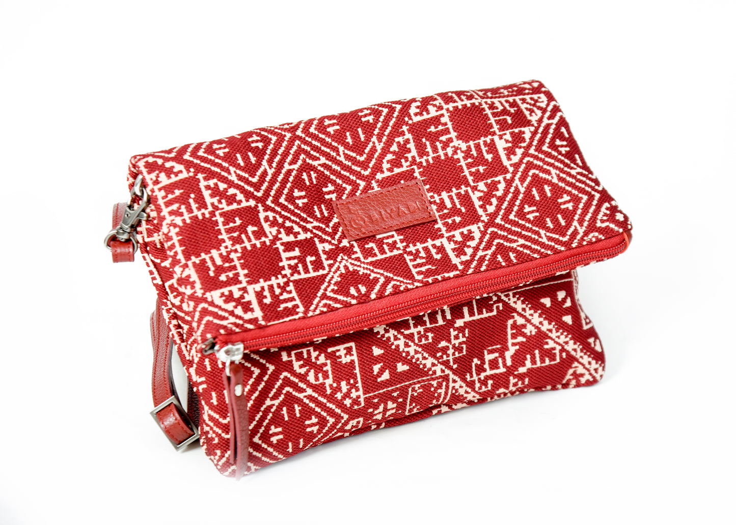 Sac bandoulière rouge en tissu marocain tissé, ornée d’un motif géométrique inspiré des broderies traditionnelles de Fès, avec fermeture zippée et finitions en cuir, création exclusive Biyadi Collection fabriquée au Maroc.