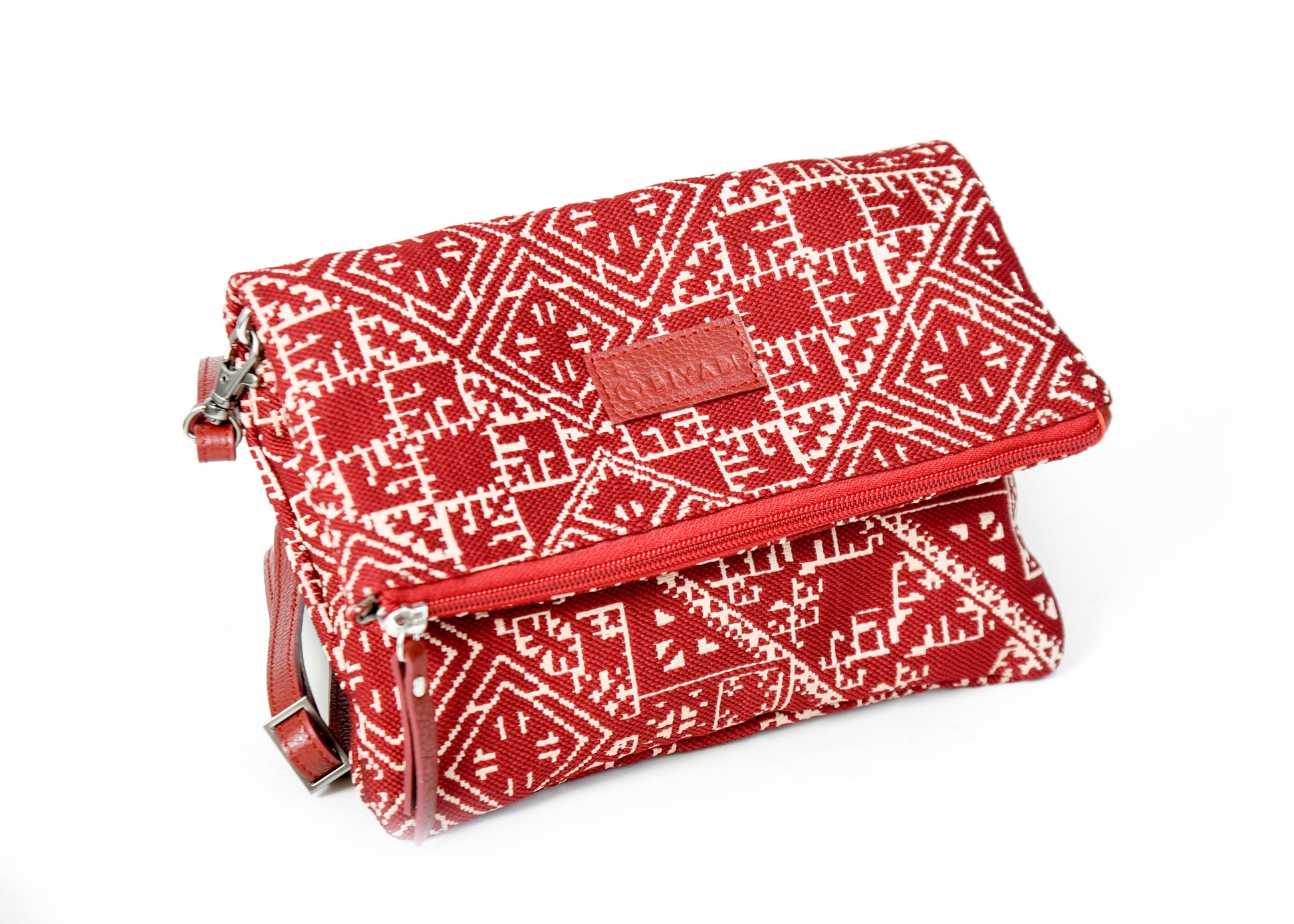 Sac bandoulière rouge en tissu marocain tissé, ornée d’un motif géométrique inspiré des broderies traditionnelles de Fès, avec fermeture zippée et finitions en cuir, création exclusive Biyadi Collection fabriquée au Maroc.
