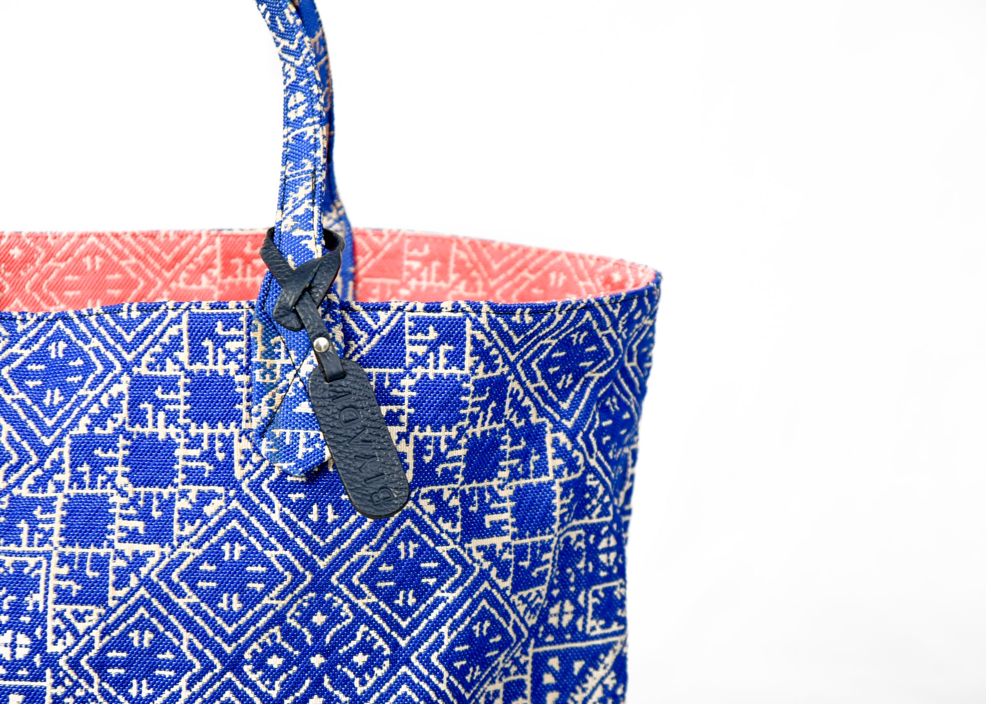 Détail du sac cabas reversible bleucobalt et corail en tissu marocain tissé avec anse en cuir noir et étiquette en cuir Biyadi Collection.