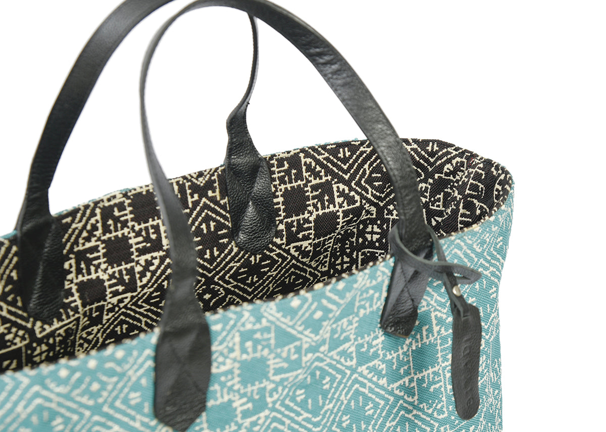 Détail du sac cabas reversible noir et turquois en tissu marocain tissé avec anse en cuir noir et étiquette en cuir Biyadi Collection.