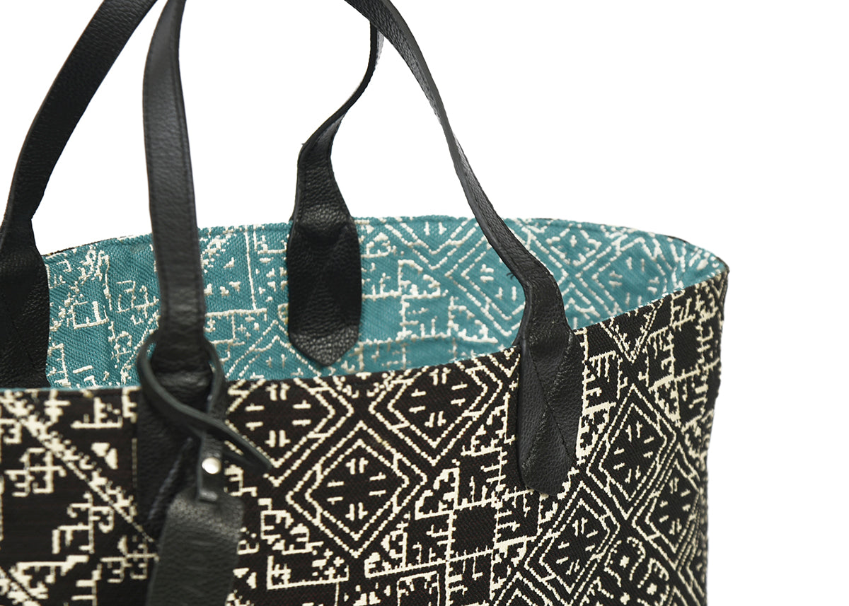 Détail du sac cabas reversible noir et turquois en tissu marocain tissé avec anse en cuir noir et étiquette en cuir Biyadi Collection.