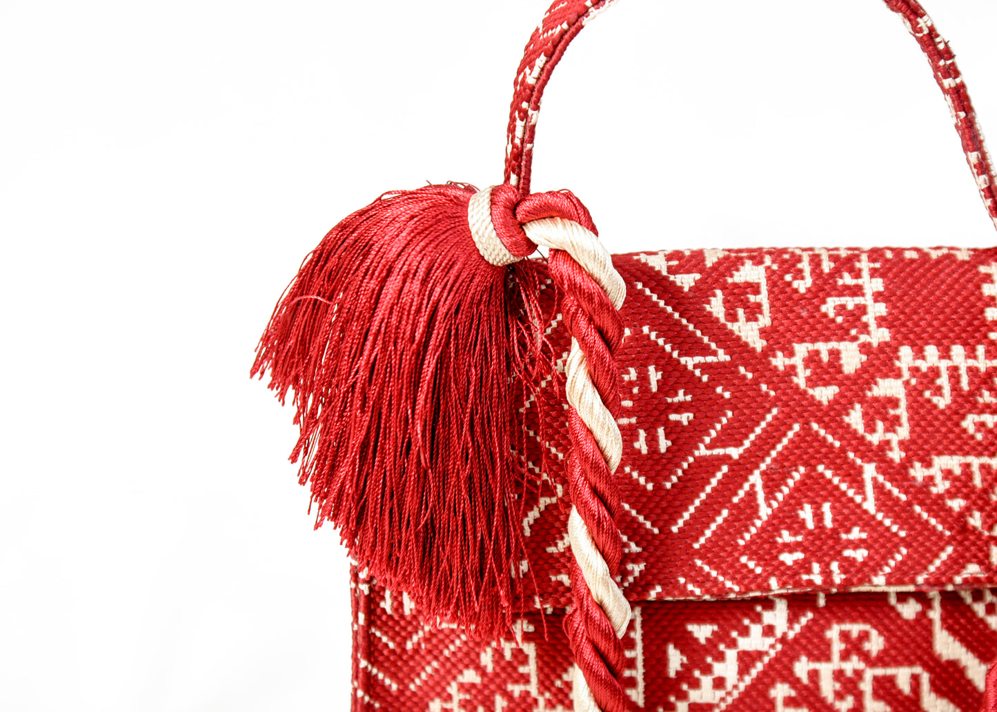 Détail du pompon bordeau et du tressage décoratif sur un sac à main en tissu marocain noir et écru tissé au Maroc.